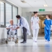 Senior female woman patient in wheelchair sitting in hospital corridor with Asian Indian male doctor and female nurse colleagues