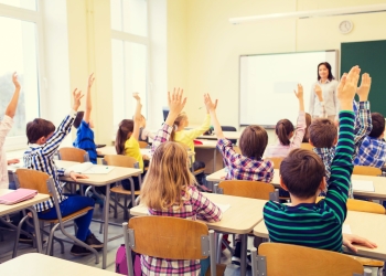 education, elementary school, learning and people concept - group of school kids with teacher sitting in classroom and raising hands
